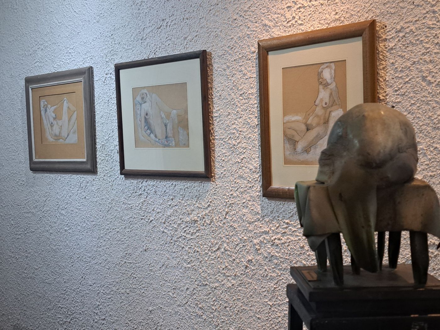 Estudios de figura enmarcados junto a una escultura en el interior del taller, sobre una pared texturada