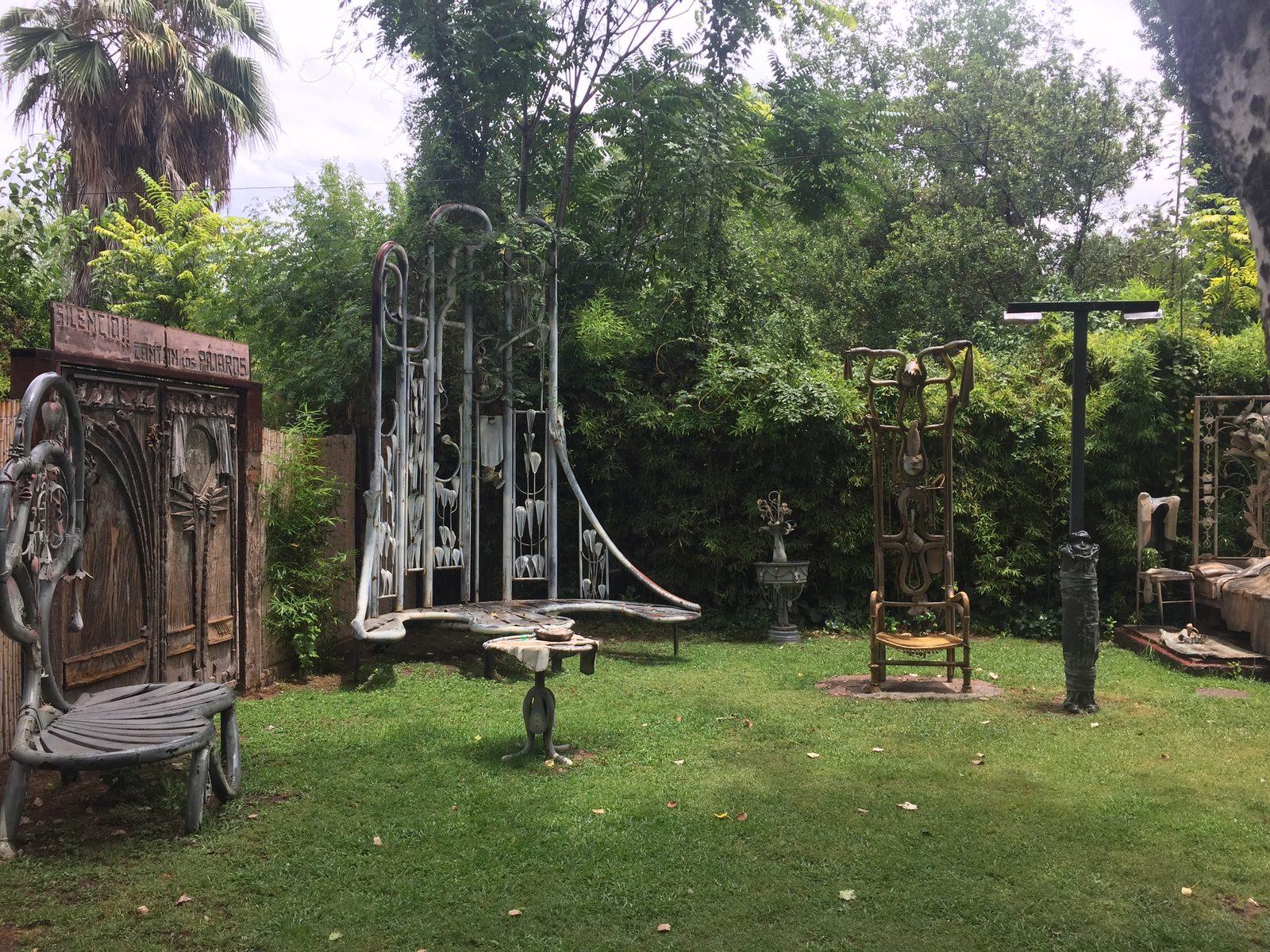 Jardín de la casa con muebles y estructuras de hierro forjado entre la vegetación