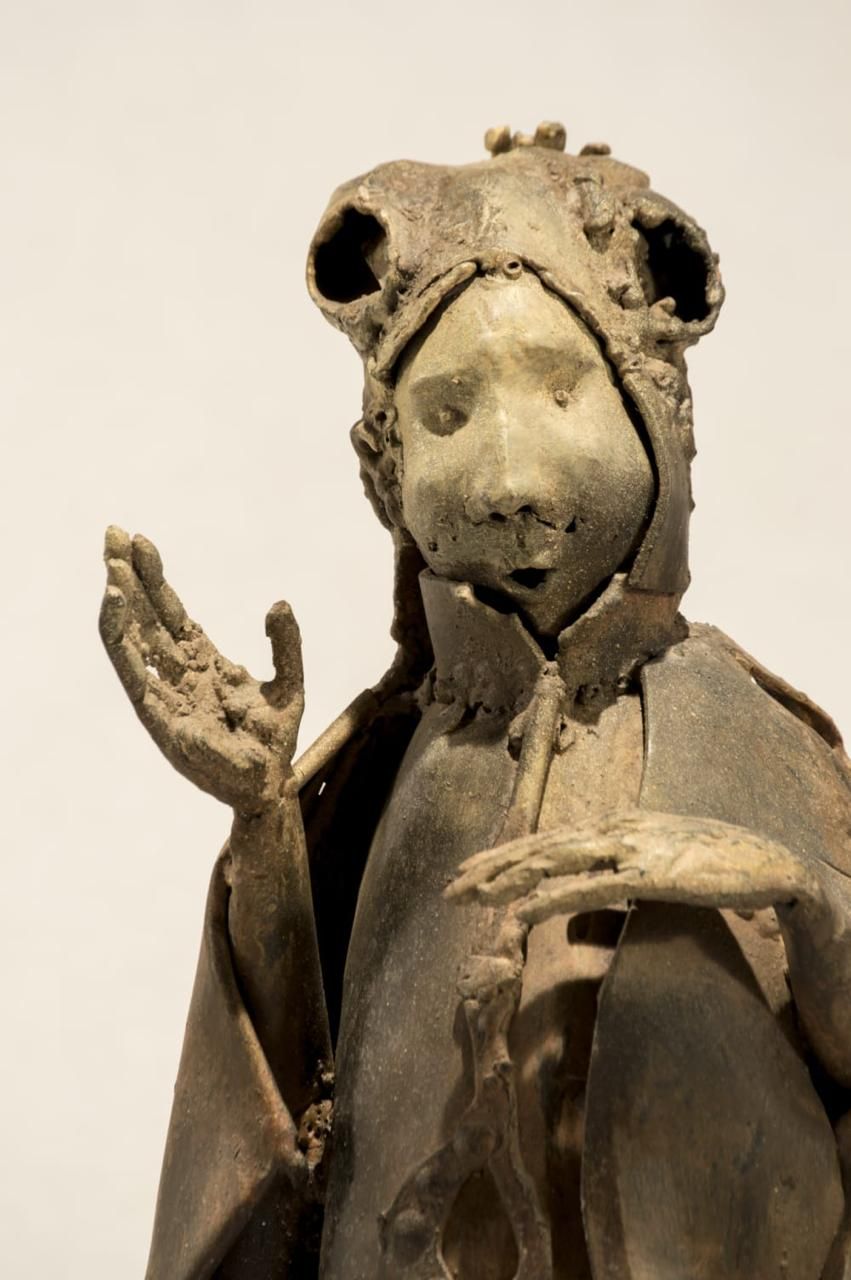 Figura con capa y tocado ornamentado, con una mano extendida hacia adelante
