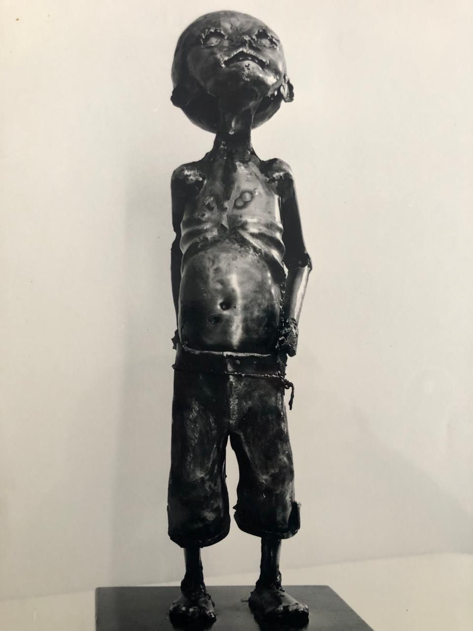 Figura infantil de pie, con cabeza esférica y manos entrelazadas